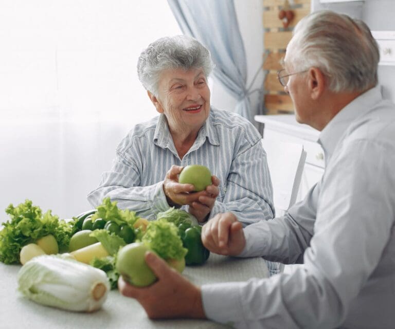 Twee mensen met artrose zitten aan een tafel met groenten die veel vitamine k bevatten.